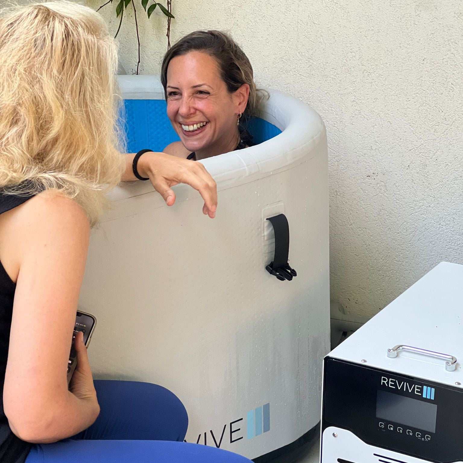 Two women enjoying a durable inflatable plunge pool with temperature control and filtration system next to a portable sauna heater unit