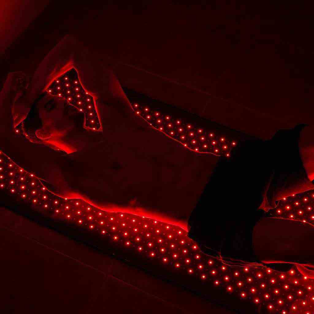 Man lying on Nushape Red Light Therapy Mat with glowing red LEDs for full-body healing and recovery