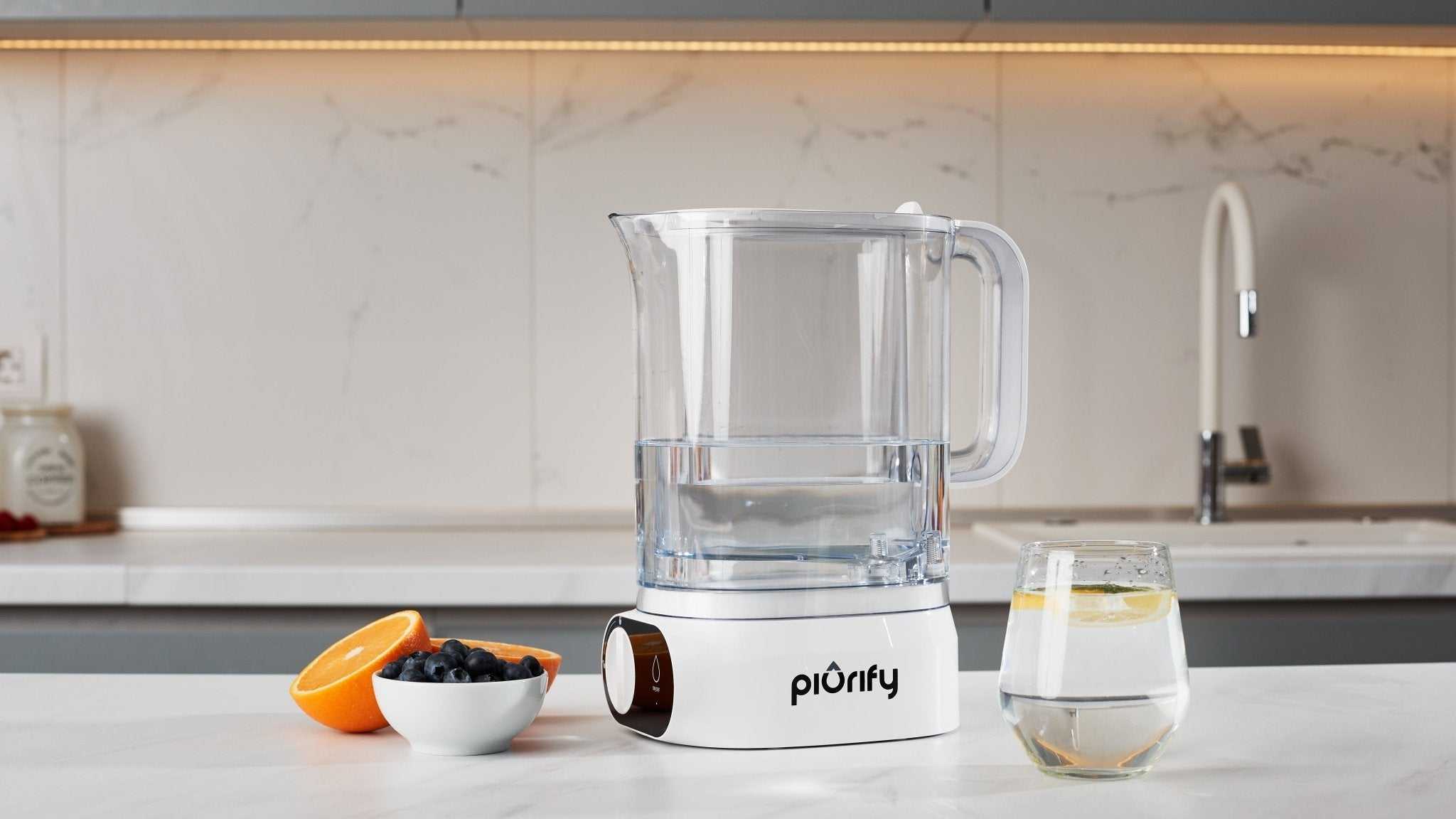 ALCHEMY® Electric Filter Pitcher on kitchen counter with clear water and fruit bowl nearby