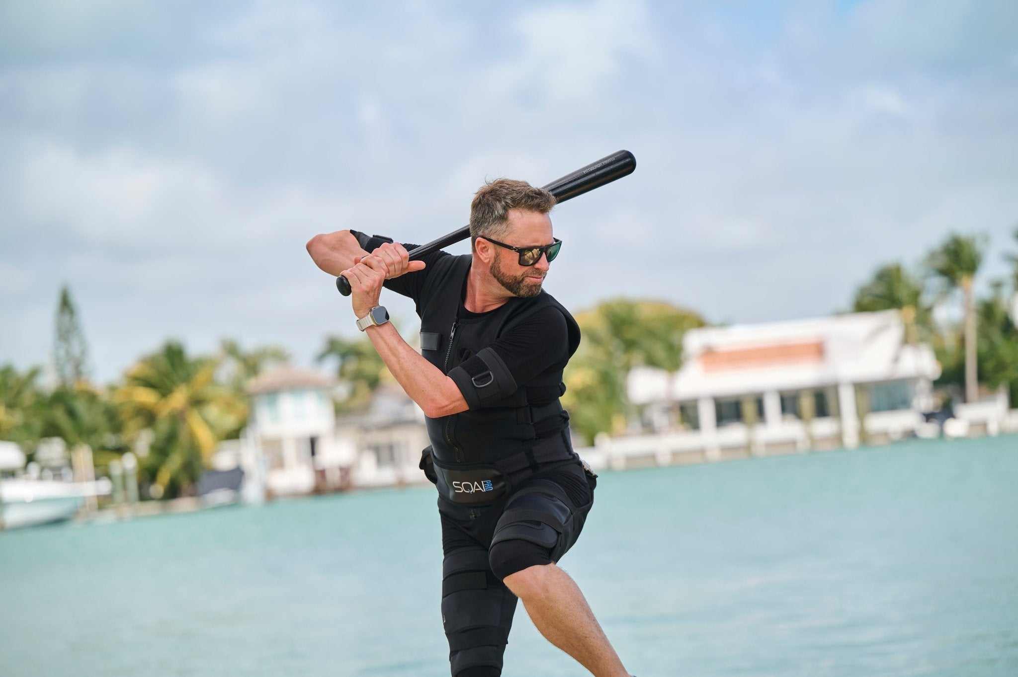Man wearing SQAI EMS training suit playing baseball outdoors near water