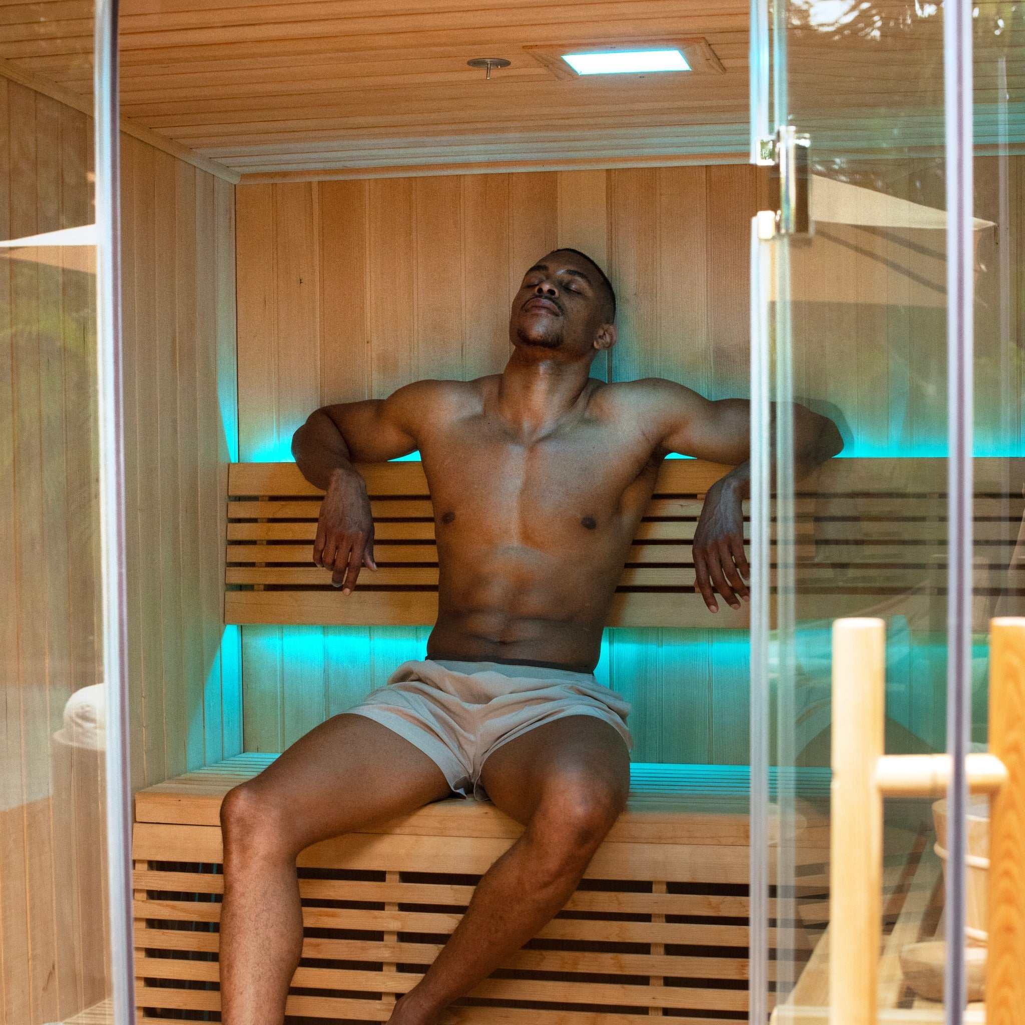 Man relaxing inside spacious 6 person traditional sauna with LED lighting and wooden benches