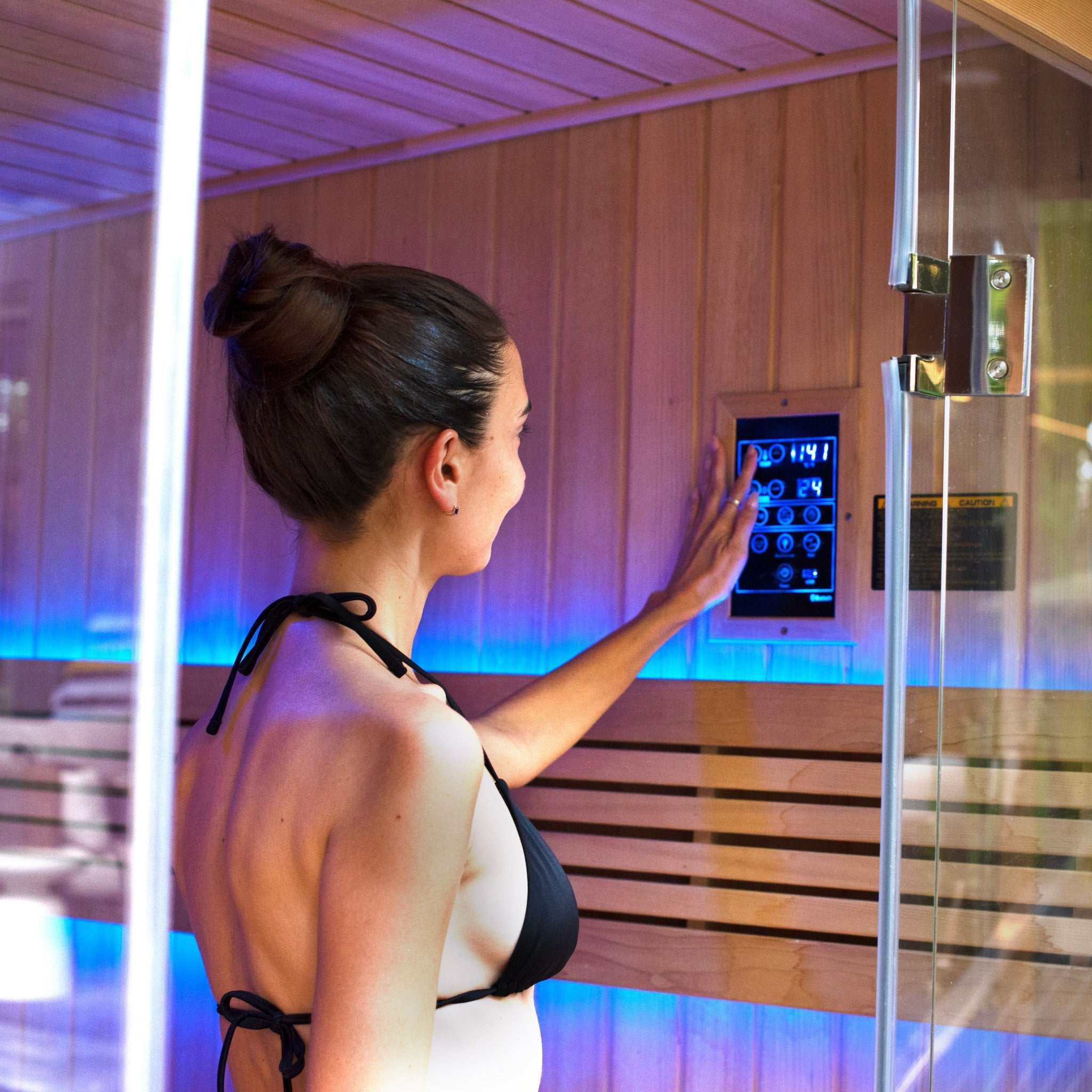 Woman adjusting control panel inside 6 person traditional sauna with Hemlock wood interior and LED lighting