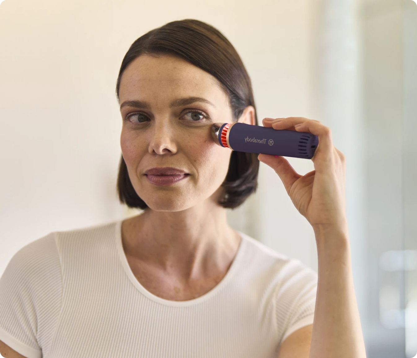 Woman using TheraFace Depuffing Wand for under-eye puffiness reduction and radiant skin enhancement
