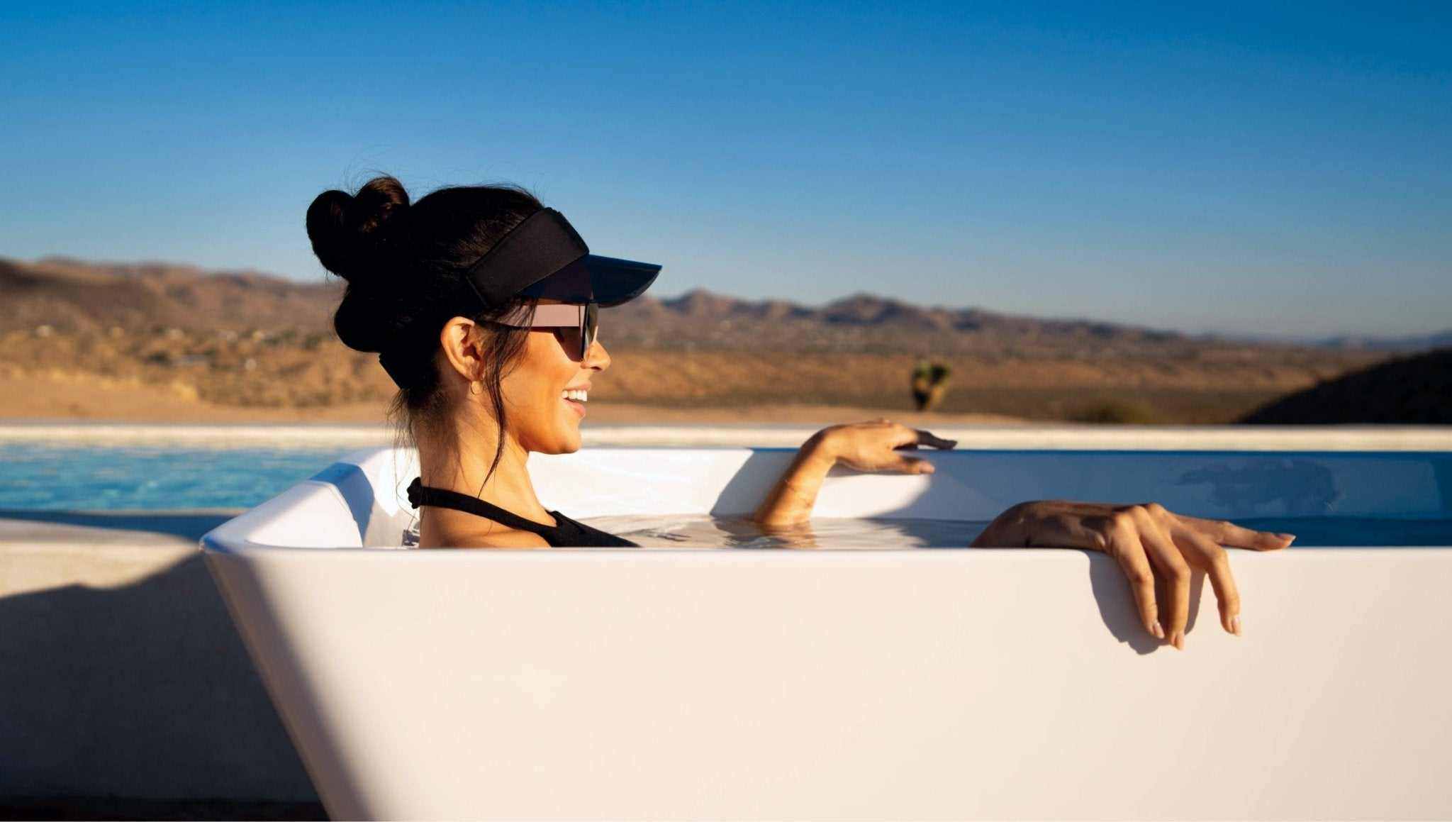 Woman relaxing in a premium gray stainless steel cold plunge tub outdoors for recovery and wellness