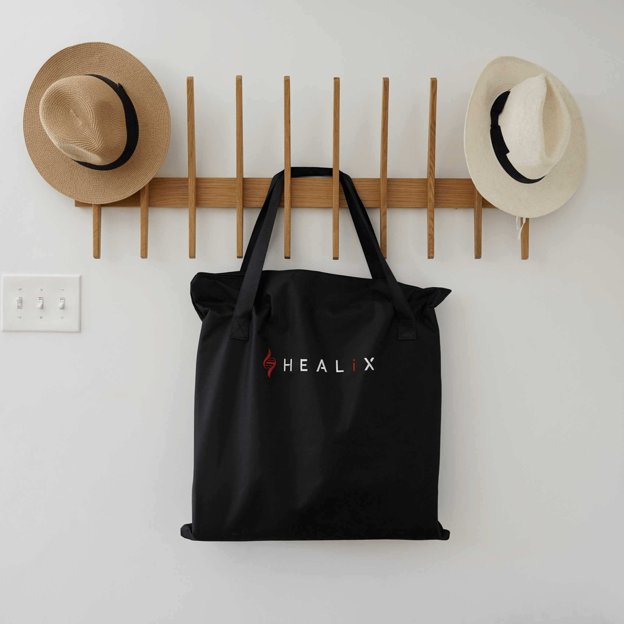 HEALiX Revive Mini portable PEMF, far infrared and red light therapy mat in black carrying bag hanging on a wall rack with hats