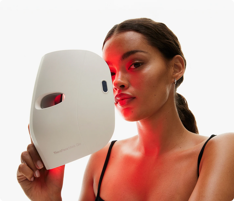 Woman holding TheraFace Mask Glo cordless LED light mask with red light therapy on face