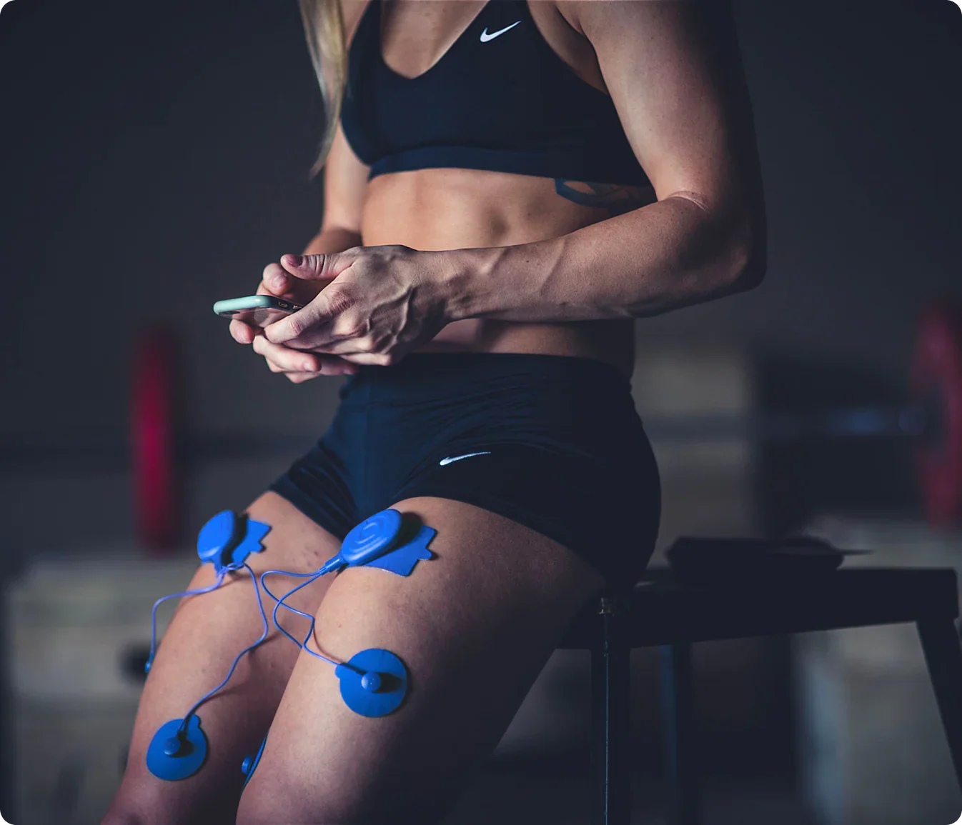 Woman using PowerDot 2.0 Duo app controlled TENS and NMES muscle stimulator on thighs