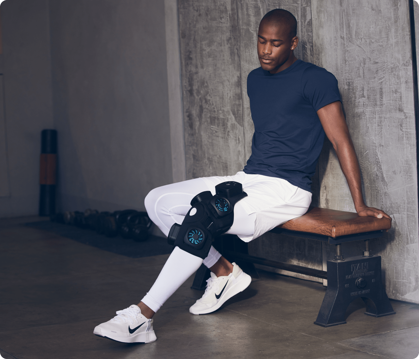 Man wearing RecoveryTherm Knee wrap with heat, cold, contrast, and vibration therapy sitting on bench