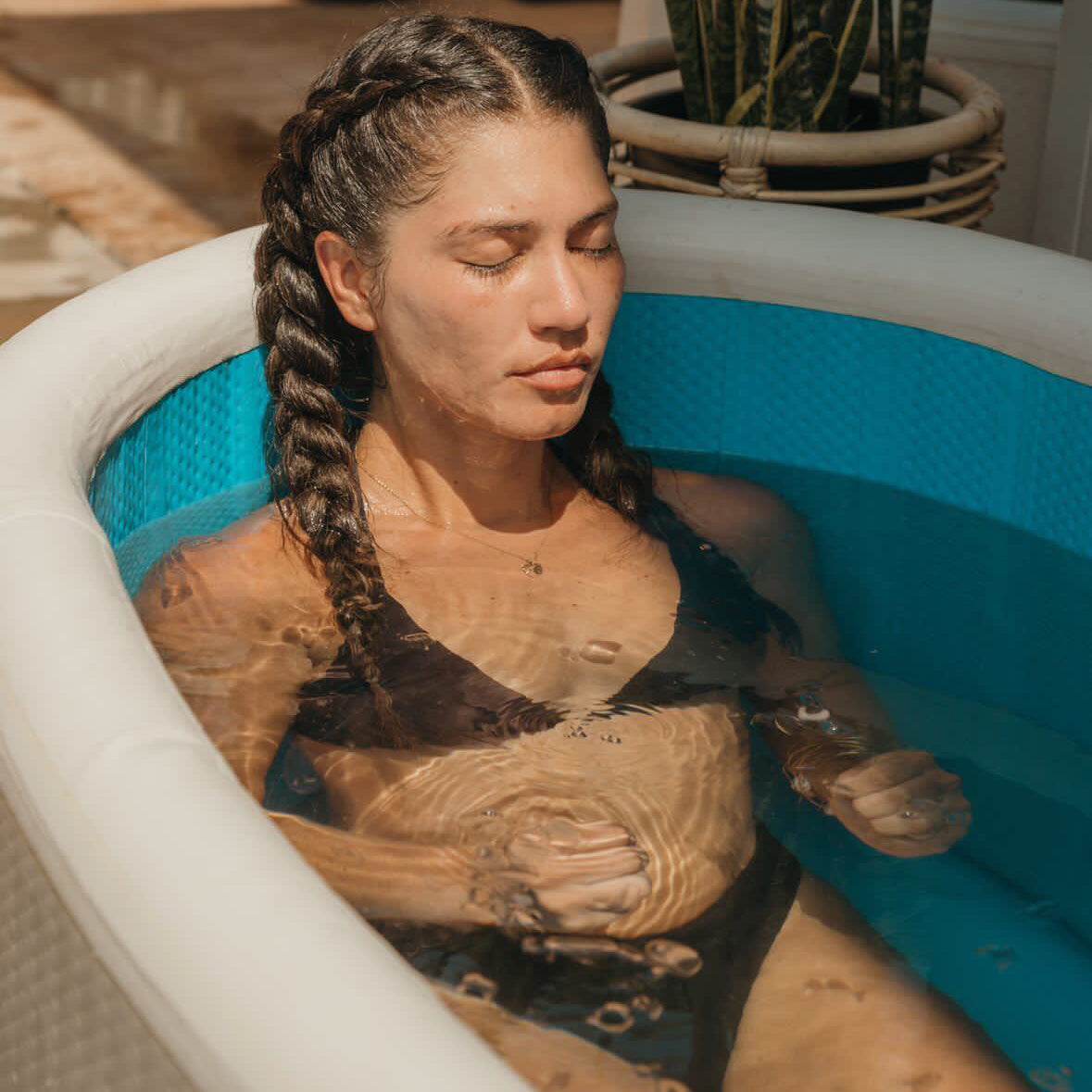 Woman relaxing in a 6 person inflatable plunge pool with temperature control and durable PVC construction, complementing a traditional sauna experience