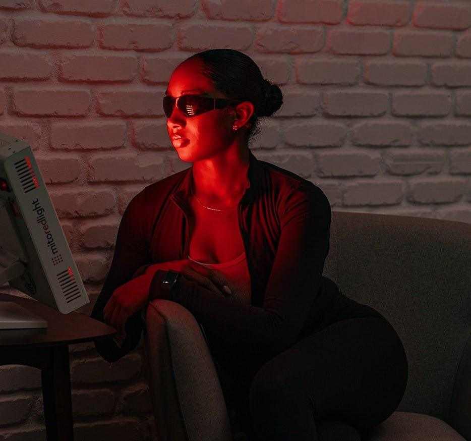 Woman using MitoPRO+ red light therapy panel emitting red light therapy indoors