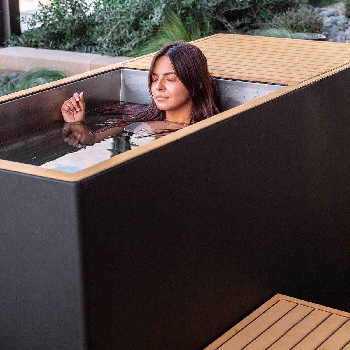 Woman relaxing in a luxury plunge ice-cold therapy tub with sleek insulated stainless steel design outdoors