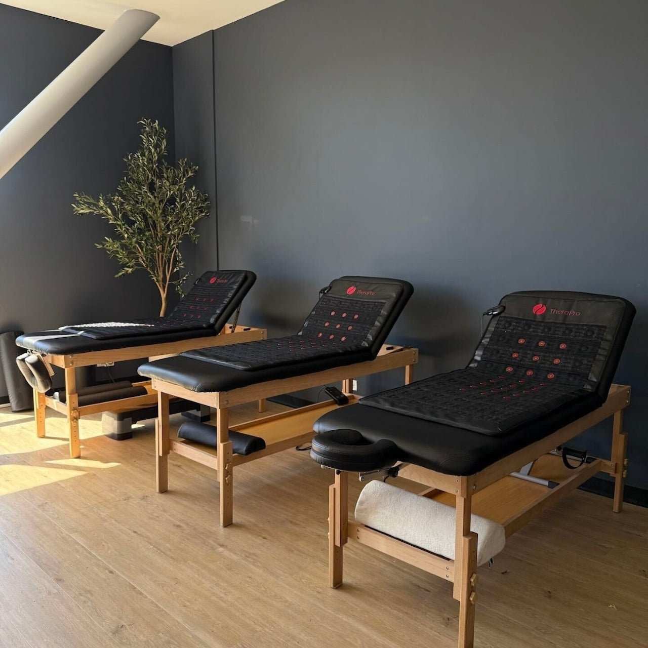 Three Therapro PEMF infrared red light healing pads on wooden treatment tables in a wellness room