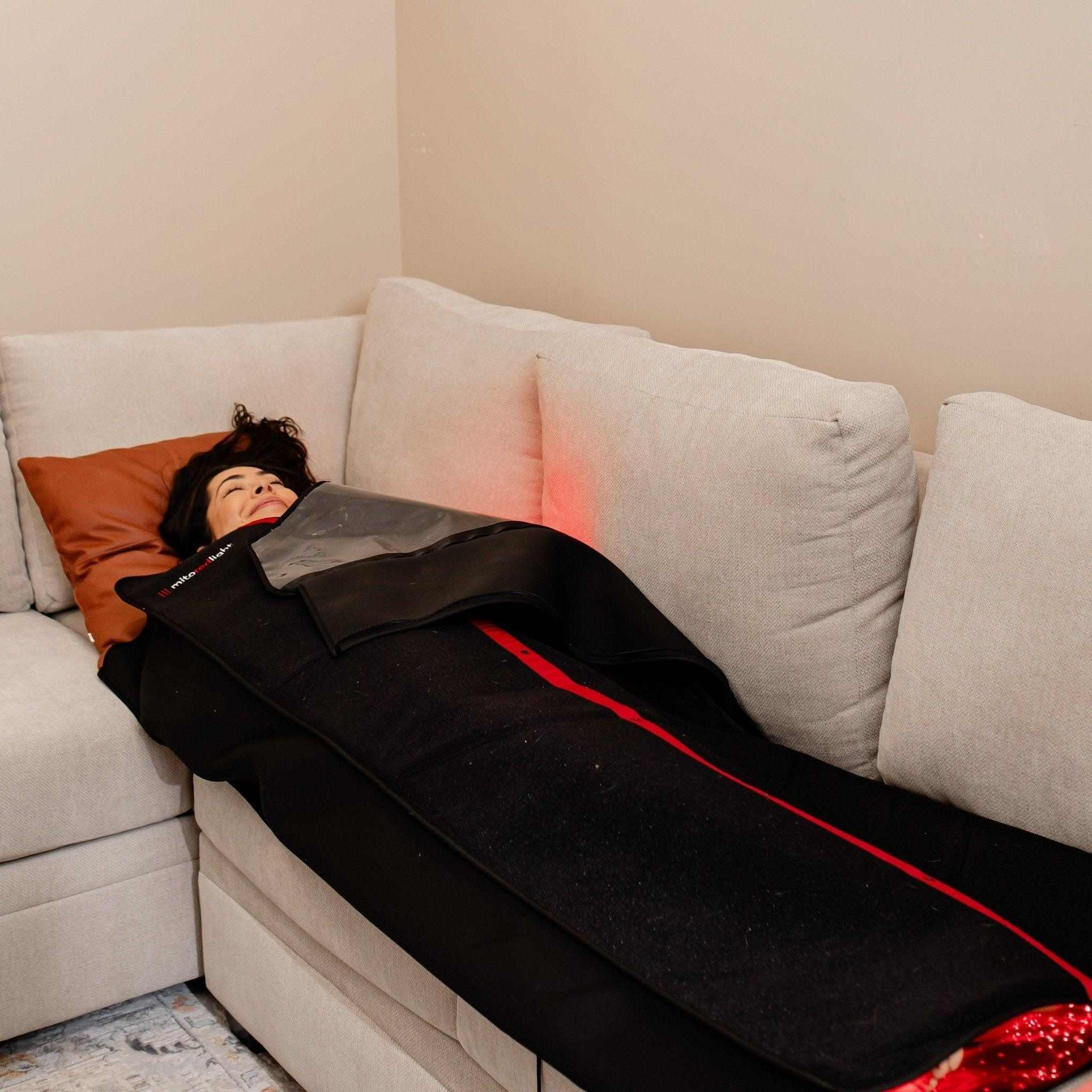 Woman using MitoPOD™ portable full body red light therapy wrap on couch