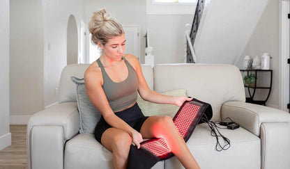 Woman using MitoQUAD Wavelength Belt for red light therapy on her leg at home